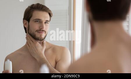 Angenehmer junger hübscher Kaukasischer Mann, der feuchtigkeitsspendende Lotion anwendet. Stockfoto