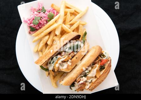 Ansicht von oben auf gestapelte und geschichtete Käsesteak-Sandwiches, die in zwei Hälften geschnitten wurden, um den Querschnitt der Zutaten zu zeigen, die mit pommes frites serviert werden. Stockfoto