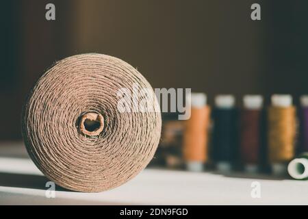 Ball aus beigefarbenem Faden auf Tisch mit bunten Verwicklungen im Hintergrund. Tapfere Boden trendige Farbe Stockfoto