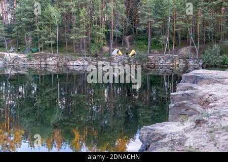 Schöne Landschaft, Camping und Zelte unter einem Pinienwald am Rande eines überfluteten Granitbruchs Stockfoto