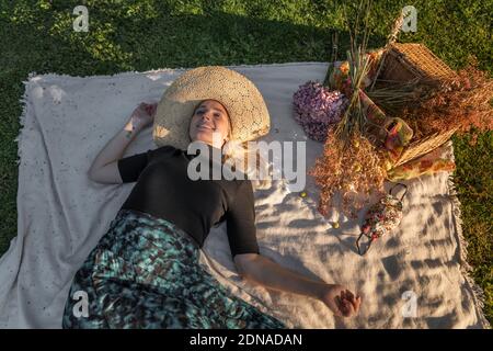 Frau, die während der Coronavirus-Sperre ein Picknick macht, mit ihrer Covid-19 Gesichtsmaske, die auf der Picknickdecke liegt Stockfoto