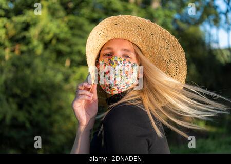 Schöne junge Frau trägt eine Coronavirus Gesichtsmaske mit einem floralen Design während Covid-19 Pandemie Lockdown Stockfoto