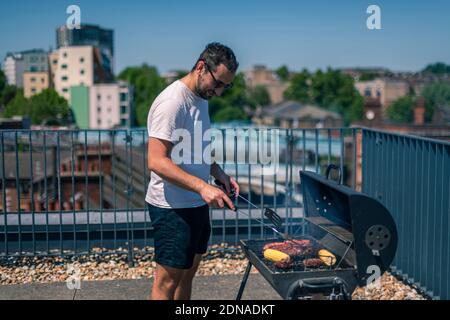 Mann kocht auf bbq, argentinisches Steak, Würstchen, Fleisch und Mais an einem Grill an einem heißen Sommertag Stockfoto