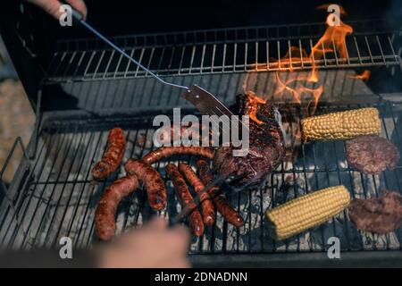 Mann kocht auf bbq, argentinisches Steak, Würstchen, Fleisch und Mais an einem Grill an einem heißen Sommertag Stockfoto