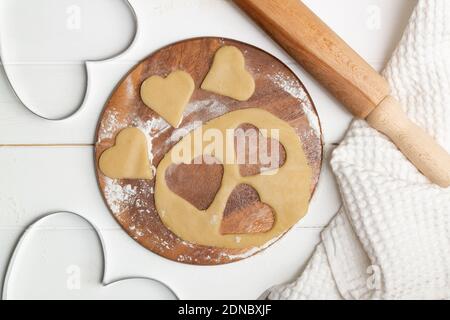 Eine herzförmige Ausschnittform und Teig schneiden Cookies neben einem Handtuch und Holzlöffel und Nudelholz. Flach liegend. Stockfoto