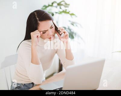 stressed young woman working on  laptop and talking on the phone in the home office Stock Photo