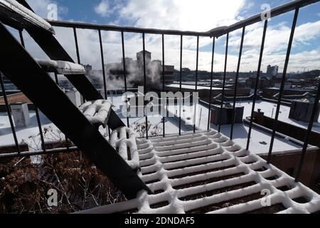 Blick von einer schneebedeckten Feuerflucht auf verschneite Dächer der Stadt und einen blauen Himmel mit hellen Wolken im Hintergrund Stockfoto