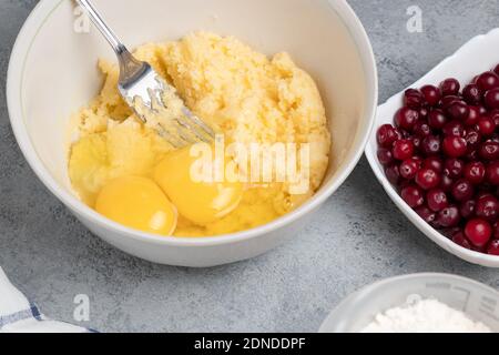Einen Teig für einen süßen Preiselbeerkuchen machen. Eier hinzufügen Stockfoto