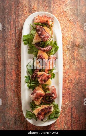 Längliches Tablett mit galizischem Octopus, mit Kartoffeln, Paprika, Olivenöl auf rustikalem Granit-Hintergrund. Konzept der spanischen ethnischen Küche. Stockfoto