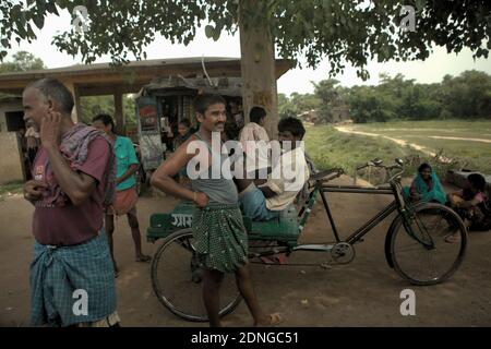 Menschen stehen, ruhen sich aus, gehen einkaufen und gruppieren sich unter einem großen Baum, wo sich ein Geschäft an der Seite einer Straße zwischen Bodh Gaya und Rajgir in Bihar, Indien befindet. © Reynold Sumayku Stockfoto