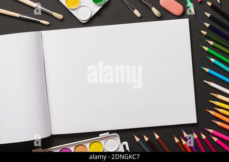 Aquarellfarben, Pinsel, Buntstifte und Skizzenbuch auf dunklem Hintergrund mit Kopierfläche, Draufsicht. Stockfoto