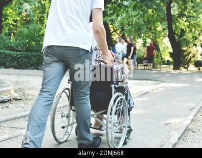 Junger Mann, der einen Rollstuhl schiebt, in dem eine behinderte Frau sitzt. Stockfoto