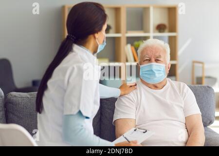 Arzt, der zu Hause einen älteren Patienten besucht und ihn während einer Coronavirus-Pandemie unterstützt Stockfoto