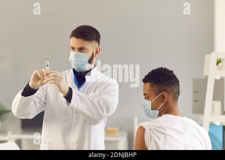 Junger Arzt in Gesichtsmaske Vorbereitung Spritze vor der Verabreichung von Impfstoff Zum Patienten Stockfoto
