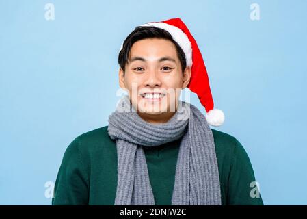 Überrascht asiatischen Mann in Weihnachten Pullover und Hut lächelnd in Hellblauer isolierter Hintergrund Stockfoto