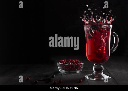 Leuchtend roter Glühwein mit Beeren und Spritzer in Glas Weinglas auf schwarzem Holztisch im dunklen Innenraum, Kopierraum. Stockfoto