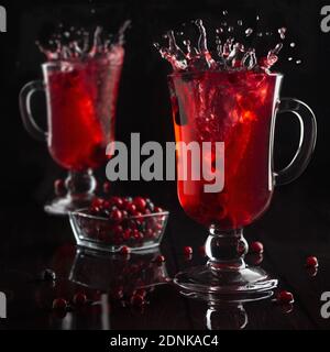 Leuchtend roter Glühwein mit Beeren und Spritzer in zwei Glas Weingläser im schwarzen dunklen Innenraum, quadratisch. Stockfoto
