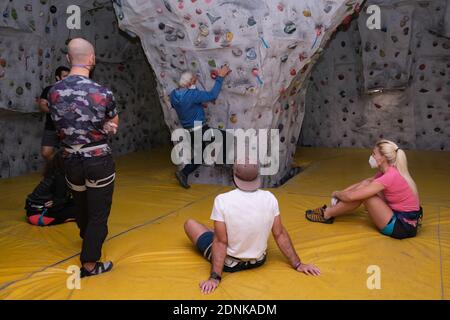 Kletterlehrer trägt eine schützende Gesichtsmaske, die seinen Schülern zeigt, wie man eine Wand erklimmt. Kletterklasse in der neuen Normalität. Stockfoto