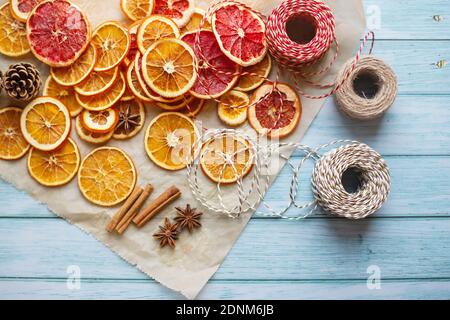 Zimt, Anis, getrocknete Orangen und Grapefruitscheiben, Fäden für diy-Projekte, Geschenkverpackung und schöne Öko-Weihnachtsdekorationen wie Kränze auf einem blauen Holztisch angeordnet Stockfoto