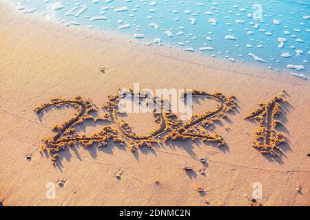 Happy New Year Konzept. Inschrift 2021 geschrieben am Sandstrand mit Welle Stockfoto