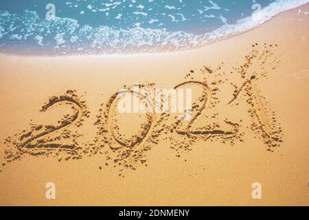 Happy New Year Konzept. Inschrift 2021 geschrieben am Sandstrand mit Welle Stockfoto