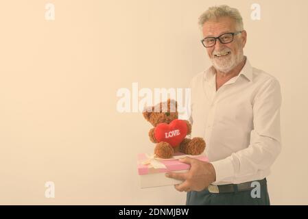 Studio shot von Happy älterer bärtiger Mann lächelnd, während sie Geschenkbox und Teddybär mit Herz und Liebe Zeichen gegen weißen Hintergrund Stockfoto