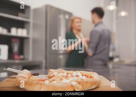 Selektiver Fokus auf köstliche frisch zubereitete Pizza, glückliches liebevolles Paar, das die Hände auf dem Hintergrund hält. Paar Vorbereitung für ein romantisches Abendessen zu Hause wit Stockfoto
