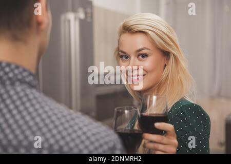 Atemberaubende glücklich blonde behaarte junge Frau lächelt an der Kamera, hält ein Glas Rotwein, mit romantischen Abend mit ihrem Mann. Glückliches Paar Celebrati Stockfoto