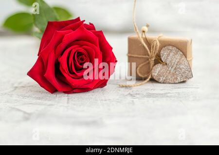 Geschenk in Bastelpapier neben roten Rose auf weißem Stein Hintergrund gewickelt. Romantisches Geschenk zum valentinstag mit Platz für Text. Konzept des Heiratsvorschlags. Weichfokus. Speicherplatz kopieren Stockfoto