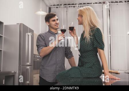 Gutaussehender Mann lächelt seine Freundin an und genießt zu Hause gemeinsam Wein. Glückliches Paar feiert Jubiläum, Toasting mit ihrer Weingasse Stockfoto