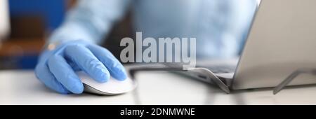 Hand in blau medizinischen Handschuh liegt auf Computer-Maus als nächstes An Brille und Laptop Stockfoto