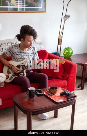 Junger Mann spielt Gitarre auf dem Sofa Stockfoto