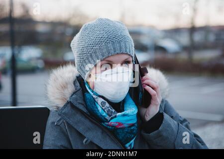 Frau trägt Schutzmaske reden über Handy Stockfoto
