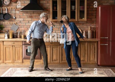 Glückliches älteres Senior liebevolles Familienpaar singen Lieder in der Küche. Stockfoto