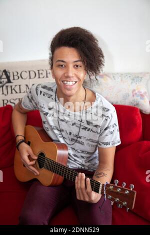 Junger Mann spielt Gitarre auf dem Sofa Stockfoto