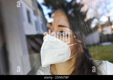 München, Deutschland. Dezember 2020. Topic picture Corona: Eine junge Frau mit Schutzmaske, Gesichtsmaske, FFP2 KN95 medizinische Maske, Community-Maske sieht besorgt aus einem Fenster in Zeiten der Coronavirus-Pandemie. MODELL FREIGEGEBEN! Quelle: dpa/Alamy Live News Stockfoto