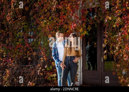 Junge schöne Paar in der Liebe in einer guten Stimmung posiert vor dem Hintergrund der roten Blätter der wilden Trauben wächst auf dem Haus. Junges Paar auf dem Par Stockfoto