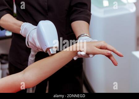 Hardware Haarentfernung Verfahren auf dem Körper des Mädchens. Ein Kosmetiker führt in einem Schönheitssalon Laserhaarentfernung auf seinem Arm durch. Hautpflege, Hardware-Kosmetik Stockfoto