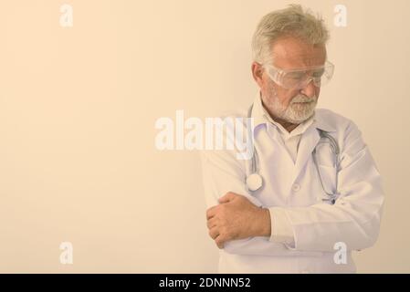 Studio shot von Sad älterer bärtiger Mann Arzt denken beim Tragen von Brillen mit Waffen gegen weißen Hintergrund gekreuzt Stockfoto