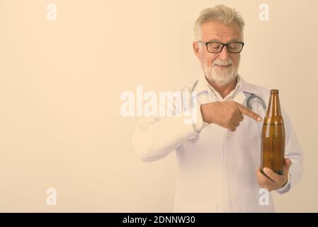 Studio shot von Happy älterer bärtiger Mann Arzt lächelnd, während sie und zeigte auf eine Flasche Bier vor weißem Hintergrund Stockfoto