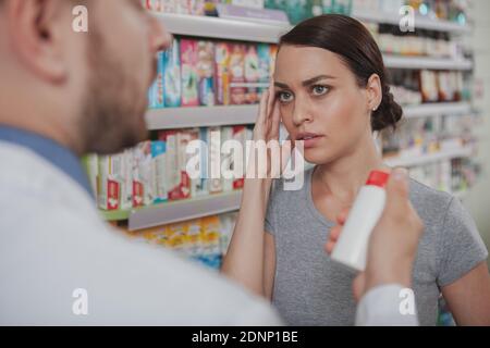 Schöne junge Frau mit Kopfschmerzen beim Einkauf von Heilmittel in der Drogerie. Schöne weibliche Kundin, die Kopfschmerzen hat und Drogen in der Apotheke kauft Stockfoto