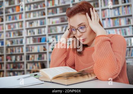 Erschöpfte Studentin beim Lesen eines Buches in der Bibliothek, Vorbereitung auf Prüfungen, Platz kopieren Stockfoto