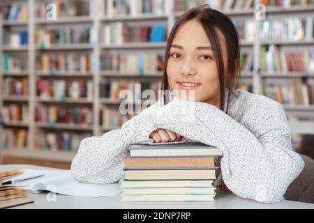 Fröhliche asiatische junge Frau lächelt die Kamera während des Studiums In der Universitätsbibliothek Stockfoto