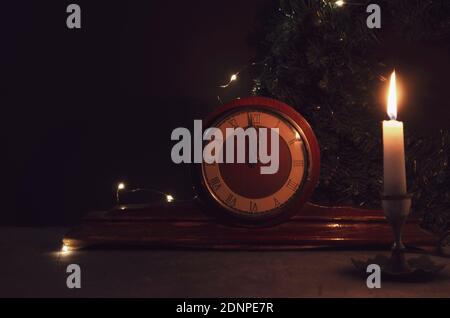Vintage alte Holzuhr, gelbe Kerze und Weihnachtsbaum Zweig auf Hintergrund. Mitternacht. Brennende Kerze. Stockfoto