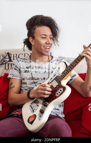 Junger Mann spielt Gitarre auf dem Sofa Stockfoto