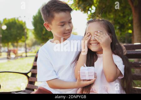 Fröhliche asiatische junge geben ein Überraschungsgeschenk an seine kleine Schwester. Entzückendes kleines Mädchen, das ihre Augen mit ihren Händen bedeckt und ein Geschenk von erhält Stockfoto