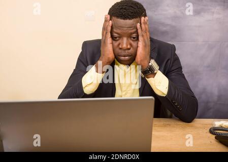 Ein junger Geschäftsmann, der am Schreibtisch saß und den Computer sah, der traurig aussass. Stockfoto