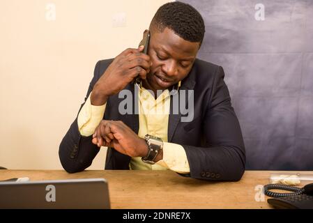 young man sitting in office suit looking at watch smiling. Stockfoto