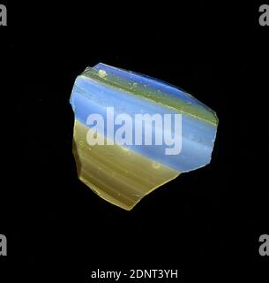 Fragment eines Gefäßes, Glas, gepresst, geschnitten, Gesamt: Höhe: 3.10 cm; Breite: 2.60 cm, Behälter, Lagerung, Küchenarbeit, frühkaiserliche Zeit, EINE leichte Krümmung des Glassfragments ermöglicht die Zuordnung zu einem Gefäß, möglicherweise einer Schüssel. Auf dem Glas sind abwechselnd blaue und braune Streifen zu sehen, auf der einen Seite zwei dünnere, auf der anderen Seite zwei dickere. Der Rücken ist braun. Für die Produktion wurden verschiedenfarbige Gläser zusammengedrückt und erhitzt. Aufgrund des komplexen Herstellungsprozesses und seiner Zerbrechlichkeit galt Glas als eines der Luxusgegenstände der Antike Stockfoto
