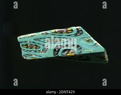 Fragment eines Gefäßes oder Glasstab, Glas, millefiori-Technik, Gesamt: Höhe: 1.90 cm; Breite: 3.20 cm, florale Ornamente, frühkaiserliche Zeit, mehrere Blumen in millefiori-Technik sind auf türkisfarbenem Hintergrund zu sehen. Es können zwei Arten unterschieden werden, von denen einer aus einem roten Punkt mit einem weißen Kern besteht, um den gelbe Punkte mit einem violetten Umriss platziert werden. Darum wird ein weiterer Kranz mit violett umrandeten weißen Punkten um ihn gelegt. Die zweite Art besteht aus einem gelben Punkt, um den violett umrandete weiße Punkte platziert werden. Stockfoto